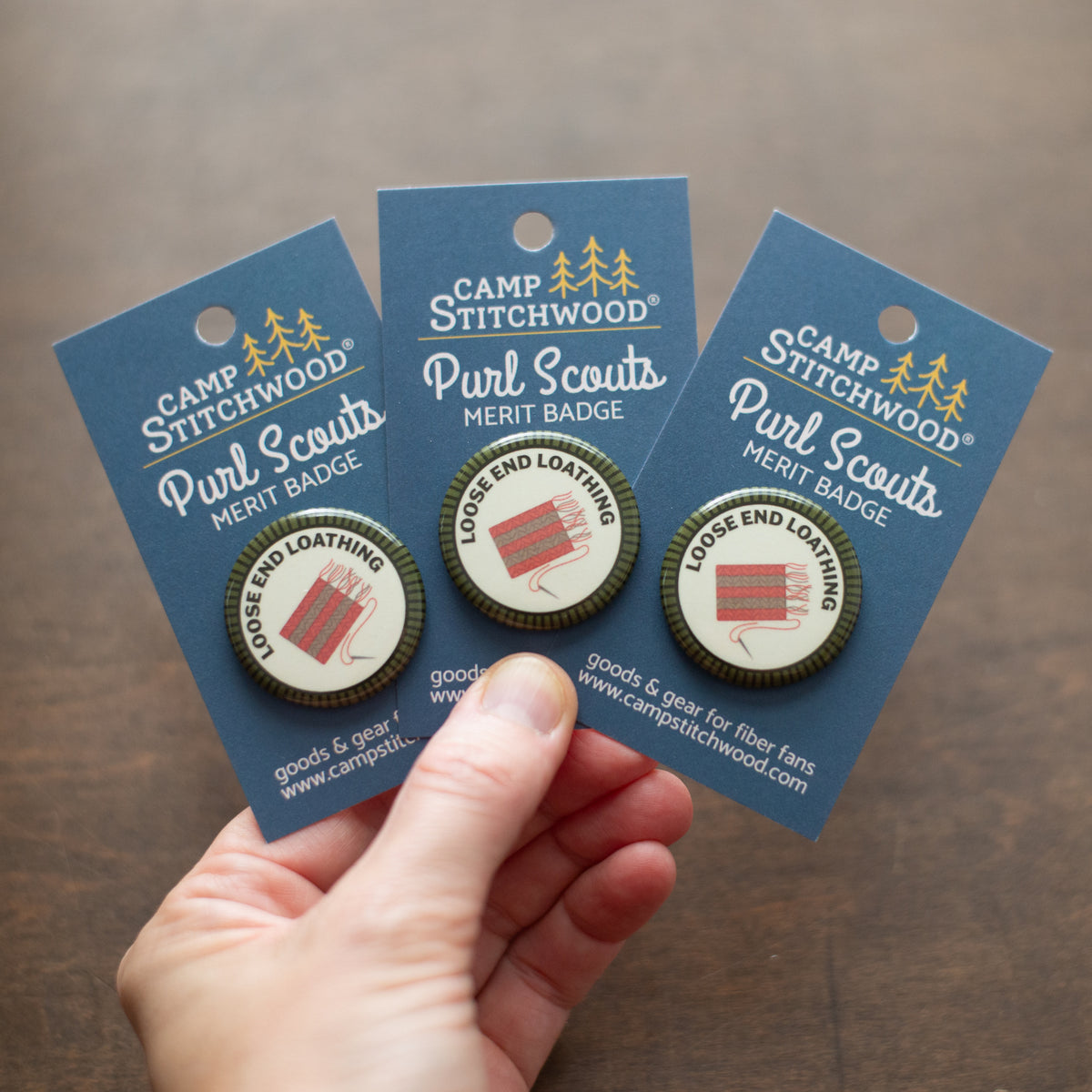 A hand holding three Loose End Loathing merit badges