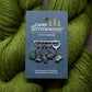 Camp Stitchwood stitch markers on a card with green yarn in the background
