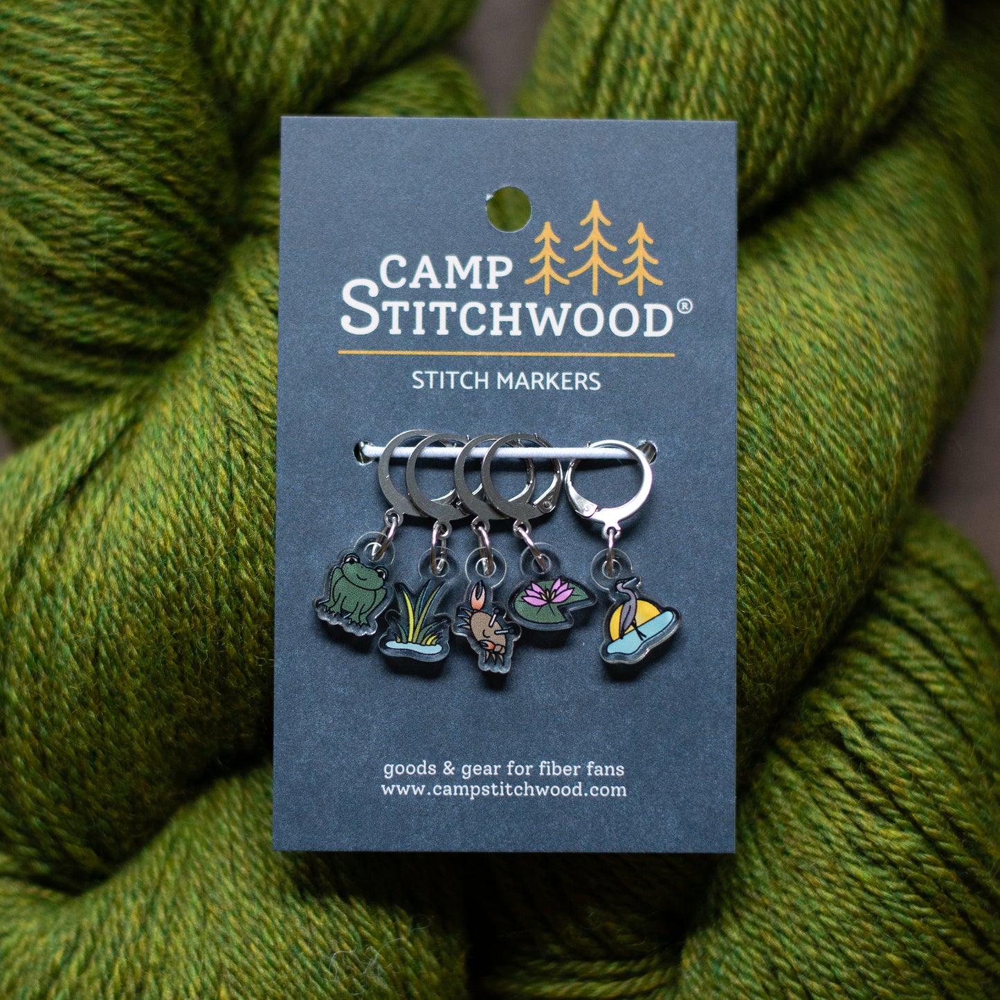 Camp Stitchwood stitch markers on a card with green yarn in the background