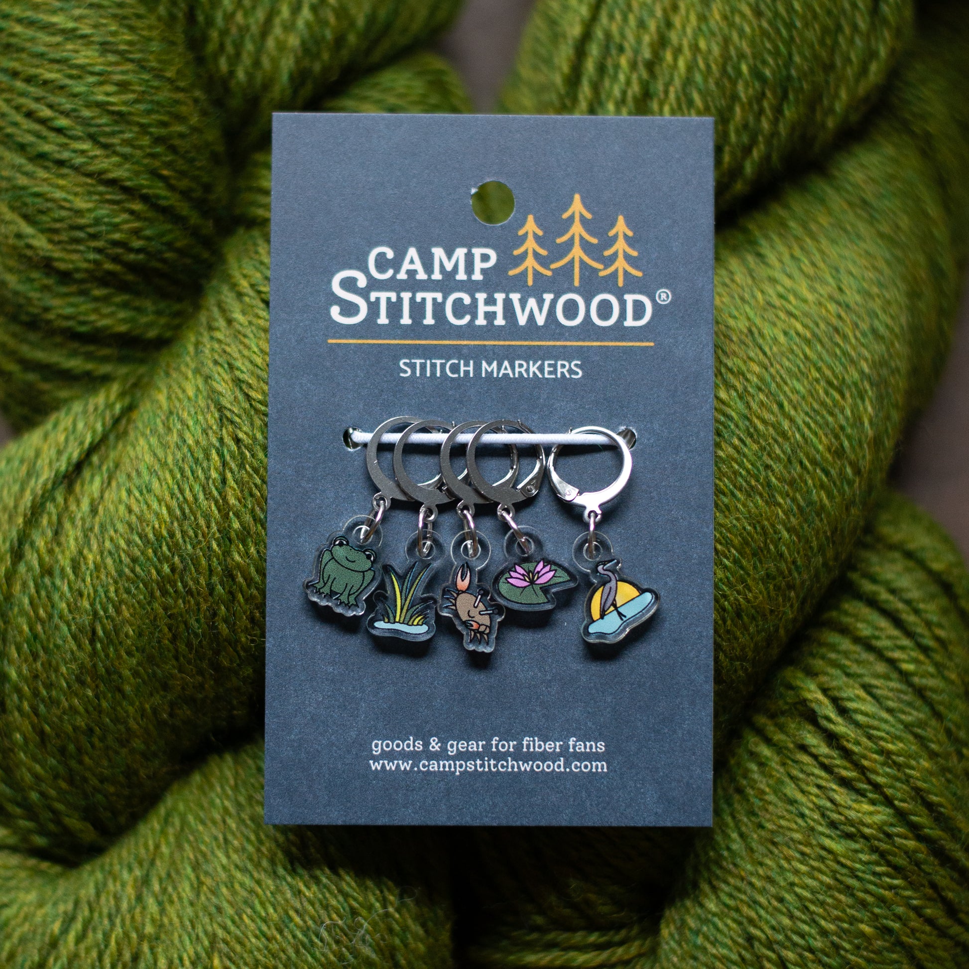 Camp Stitchwood stitch markers on a card with green yarn in the background