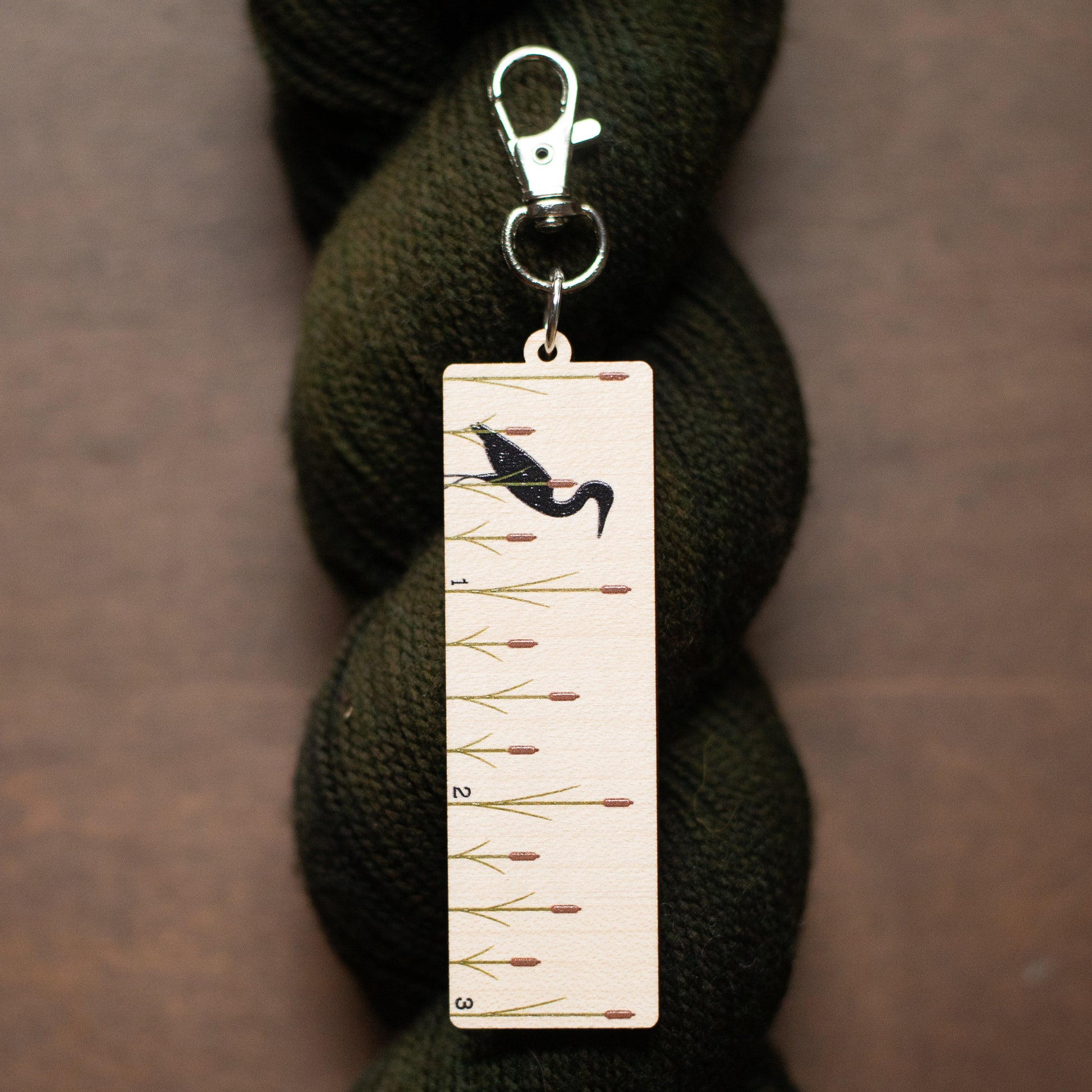 Clip on tool with ruler design and bird illustration on a skein of yarn.