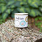 The Purl Scouts Camp Mug outside on a log