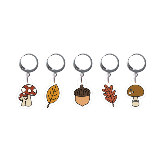 Set of five stitch markers with autumn-themed charms on a white background